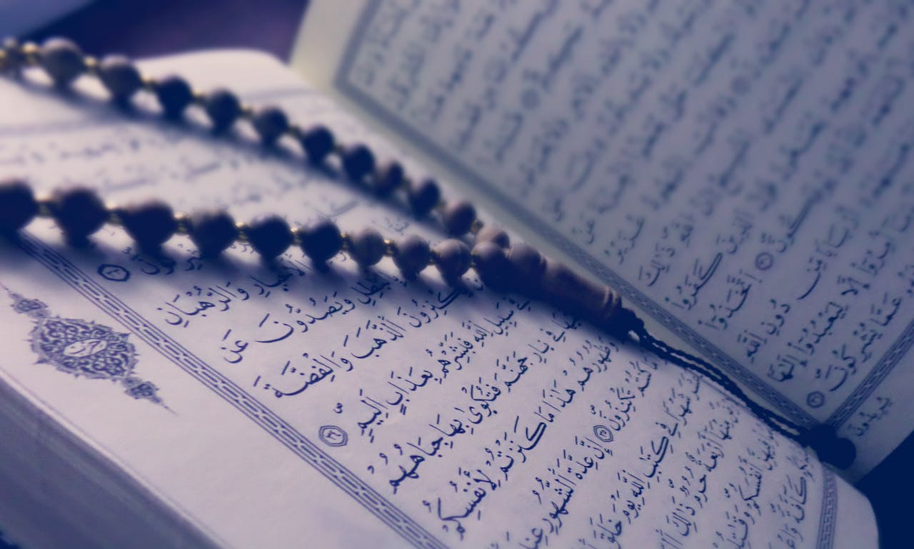 gallery-4 A close-up of prayer beads resting on an open Quran page, depicting Islamic faith and worship.