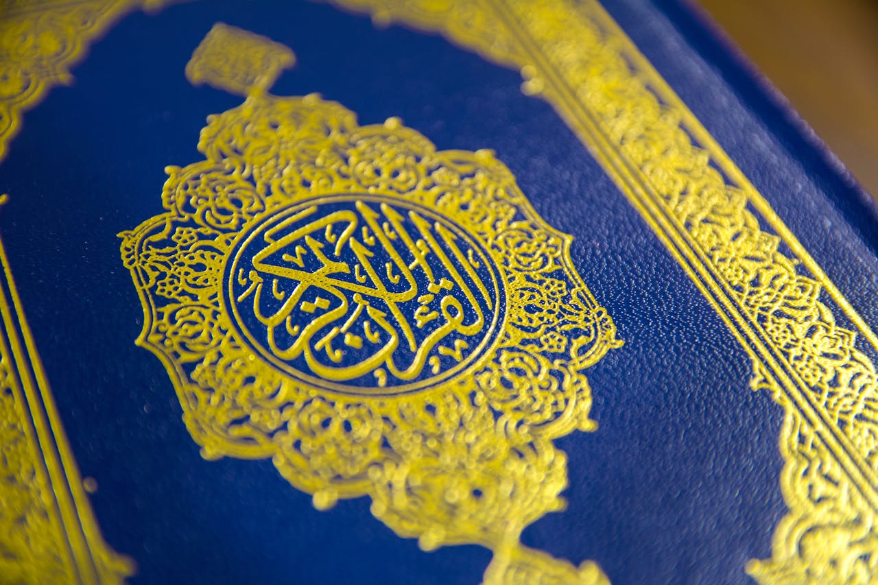 our-services-1 Close-up of intricate gold Quranic calligraphy on a blue cover, showcasing elegant Islamic design.